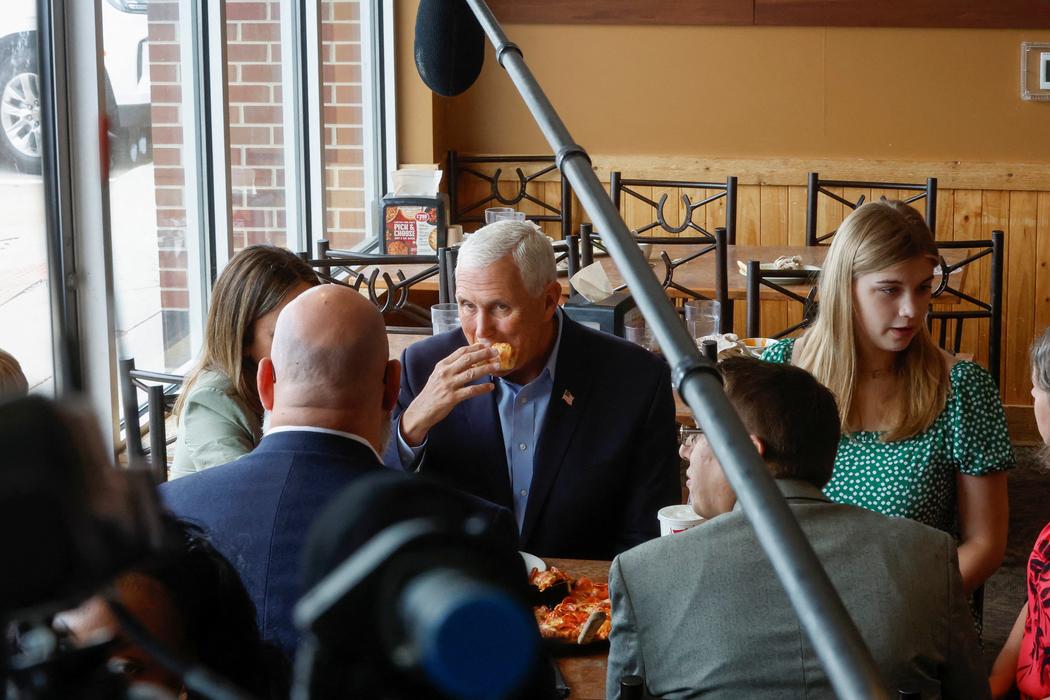 写真上は2016年の大統領選の際に「ピザ・ランチ」を訪れたトランプ前大統領（アイオワ州ウォーキーで2016年1月15日　ロイター/アフロ）。写真下は大統領選への出馬を表明した翌日にピザ・ランチを訪れ、有権者と一緒にピザを食べるペンス前副大統領。支持率低迷で10月に候補者レースから離脱した（アイオワ州ウォーキーで2023年6月8日　ロイター/アフロ）