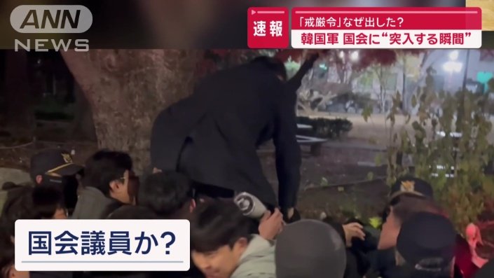 スーツ姿の男性が柵を乗り越えようとし、市民もそれを手助け