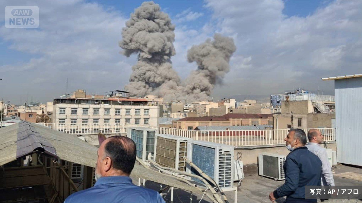 イランの首都テヘランで爆発が起こり、空に立ち上る煙を見守る人々（写真：AP/アフロ）